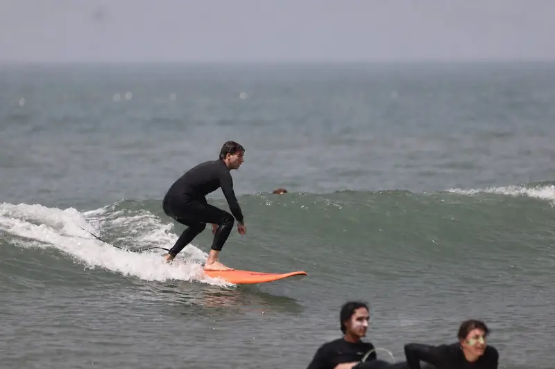 Surfer standing on an orange board riding a wave off Taghazout