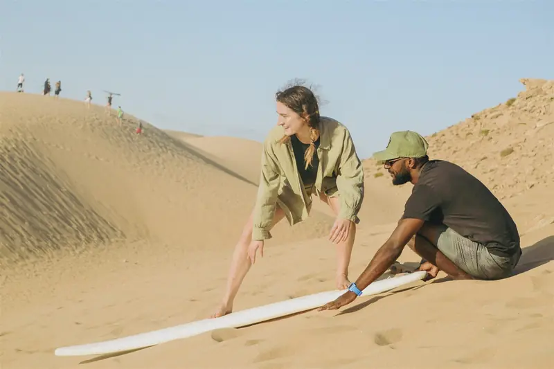 Surf coach and guest with a board on the sand dunes near Tamri